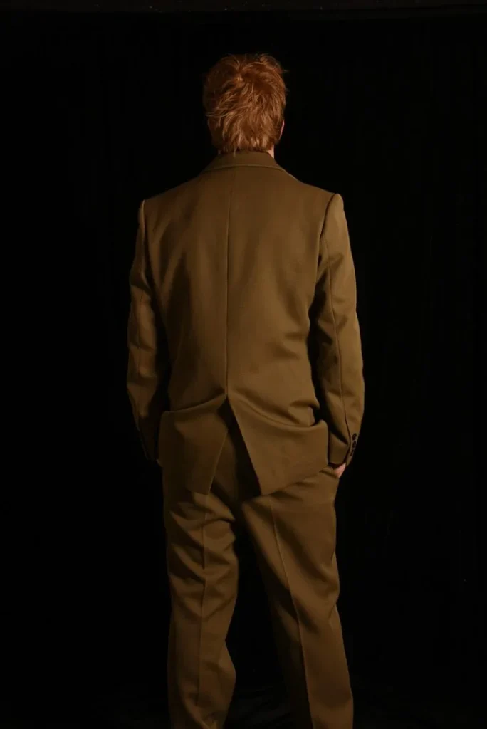 Costume marron sur mesure de Timothé Chevé porté de dos, mains dans les poches, en studio