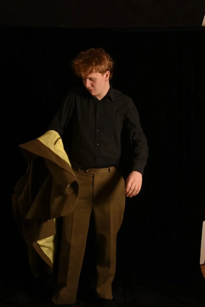 Timothé Chevé en studio, la veste de son costume marron sur mesure à la main, doublure jaune pâle visible