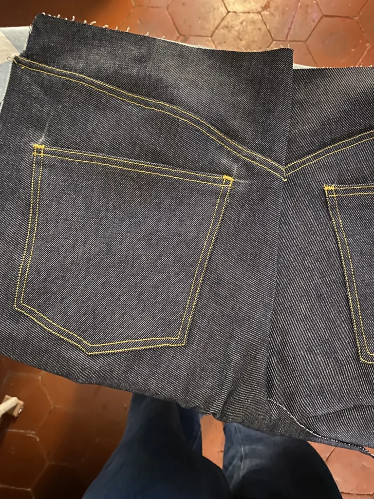Poches plaquées arrière du jean 22BB Timprod en denim brut, surpiquées de fil jaune, pendant le montage