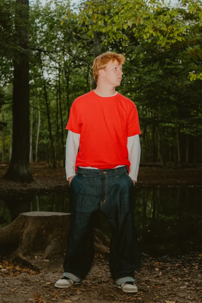 Pantalon baggy 22BB Timprod en denim brut porté avec un t-shirt rouge, mains dans les poches, en forêt