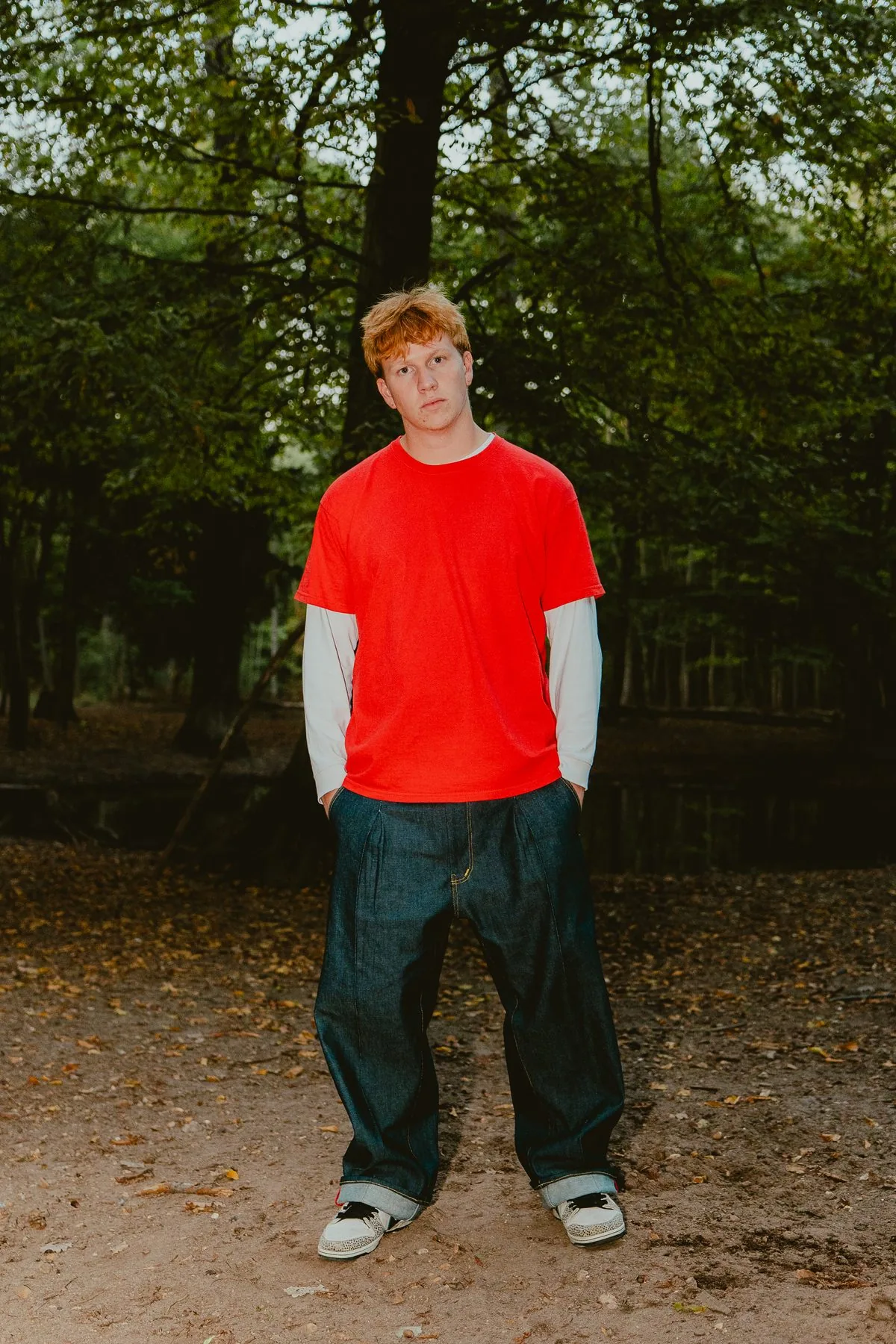 Pantalon baggy 22BB Timprod en denim brut porté de face avec un t-shirt rouge, en forêt