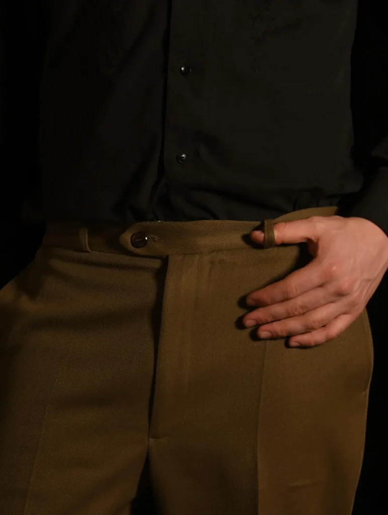 Ceinture du pantalon de costume sur mesure fermée par un bouton, la main posée sur la hanche