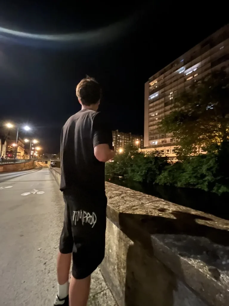 Short Timprod noir porté de nuit au bord d’un quai, logo brodé en blanc sur la poche arrière