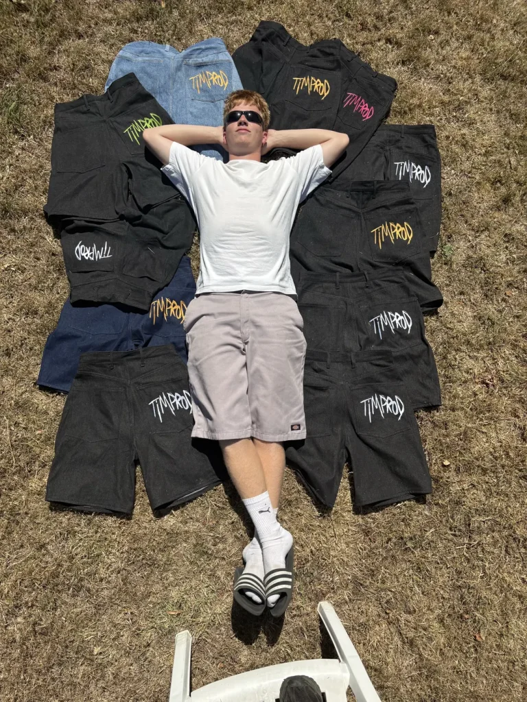 Timothé Chevé allongé sur l’herbe au milieu de la première série de shorts Timprod, logos brodés de couleur