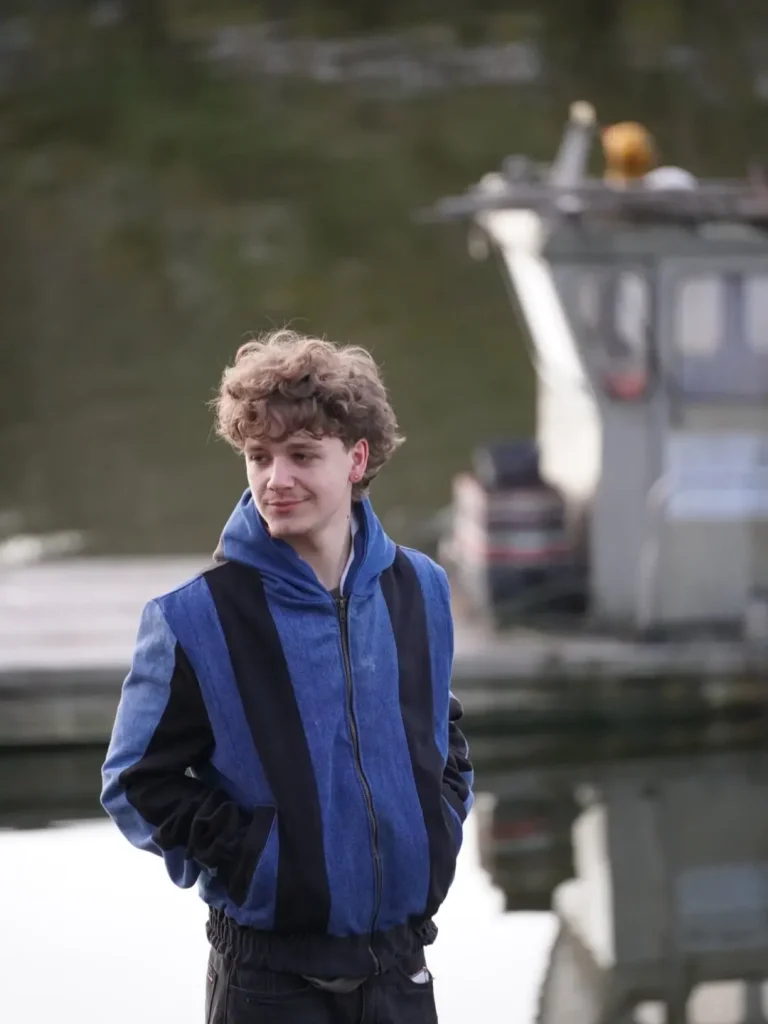Veste Timprod cousue dans des jeans recyclés, bandes de denim bleu et noir, capuche et zip, portée au bord de l’eau