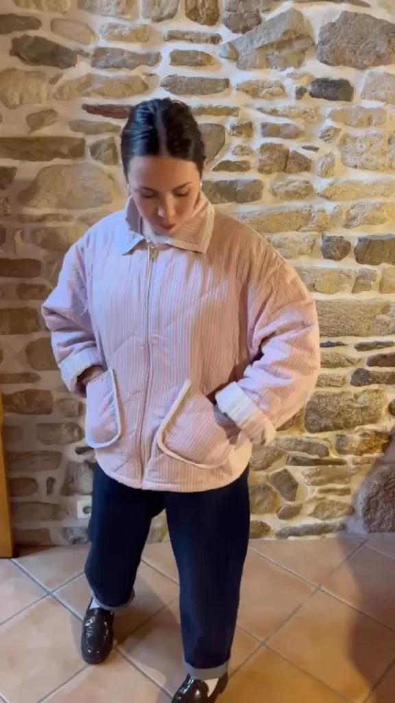 Veste matelassée cousue dans une couverture rayée rose, portée devant un mur de pierre
